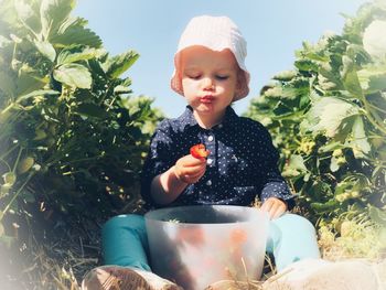 Portrait of young girl sitting on plant and eating strawberries 