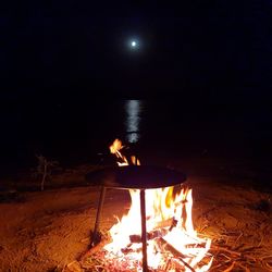 Bonfire on wooden post at beach against sky at night