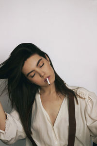 Beautiful young woman with cigarette in mouth against white background