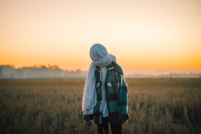 Rear view of woman standing on field against sky during sunset