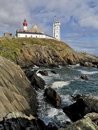 Lighthouse on rocks by sea against sky