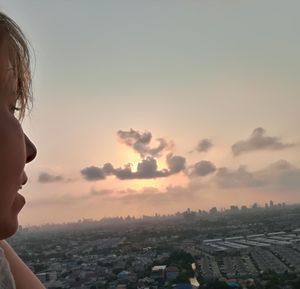 Woman looking at cityscape against sky during sunset