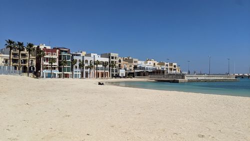 Buildings by sea against clear blue sky