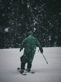 Rear view of man skiing on snow covered field during snowfall