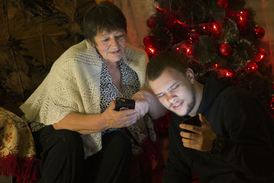 Young woman using mobile phone at christmas tree