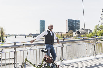 Mature man with bicycle listening to music on bridge in the city