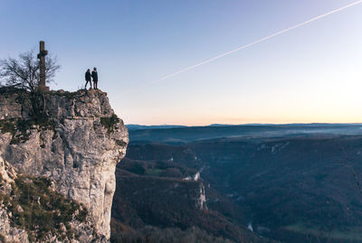 Silhouette of two people above a cliff in the evening