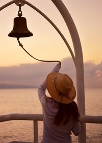 Rear view of woman holding umbrella against sea during sunset