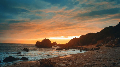 Rocks on beach against sky during sunset