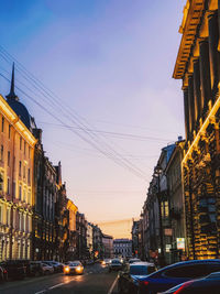 Cars on road amidst buildings against sky at sunset