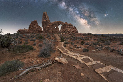 Shabby stairs path leading to turret arch located near rough canyon against glowing milky way at night sky in arches national park in utah, usa