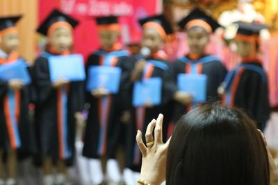 Rear view of woman against students wearing graduation gowns