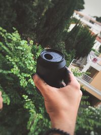 Close-up of hand holding drink against trees