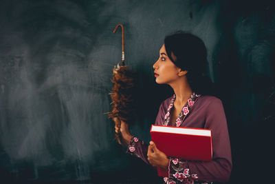 Woman holding object while standing against wall