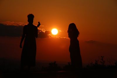 Silhouette people standing against orange sky during sunset