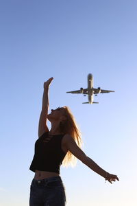 Low angle view of woman flying airplane against clear sky