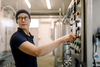 Female farmer wearing eyeglasses operating machine at dairy factory