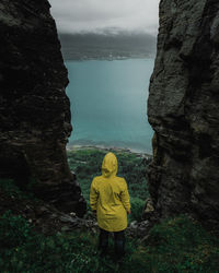 Rear view of man standing on rock by sea against sky