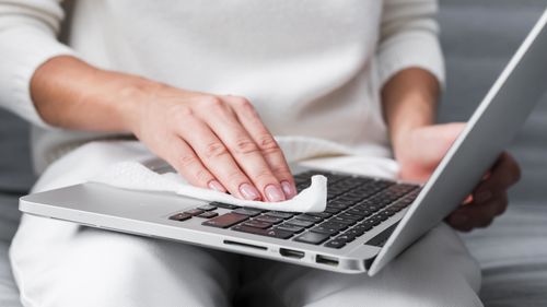 Midsection of woman cleaning laptop with paper