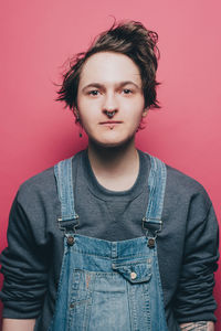 Portrait of confident male hipster wearing overalls over pink background