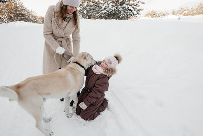 Mother and daughter playing with the dog in the winter forest