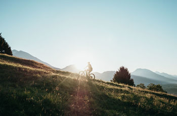 MAN RIDING BICYCLE BY MOUNTAIN AGAINST SKY