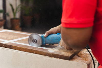 Hands of carpenter cutting piece of wood with electric circular saw.