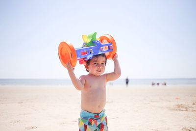 Portrait of shirtless boy carrying plastic toy on head at beach