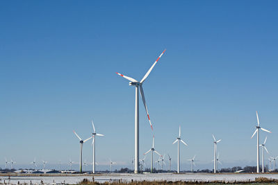 Windmills on field against clear blue sky