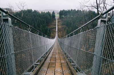 Footbridge against sky seen through chainlink fence