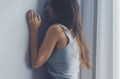 Sad woman standing by wall at home