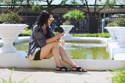 Side view of young woman sitting on retaining wall