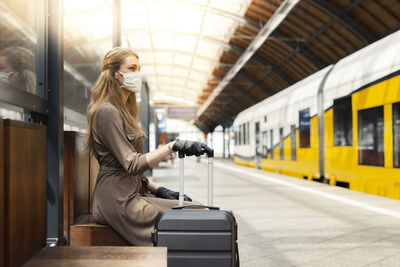 Side view of woman wearing mask sitting at railroad station