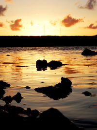 Silhouette rocks in sea against sky during sunset