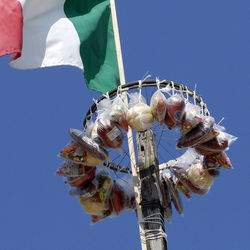 Low angle view of hand holding flag against clear blue sky