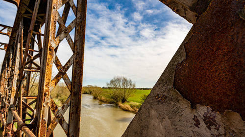 Selective focus on flaking paint on a rusty surface of bridge with river in background