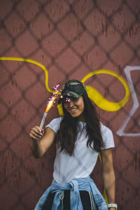 Portrait of young woman holding distress flare against wall