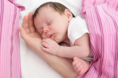 Cropped hand of mother with newborn daughter sleeping on bed