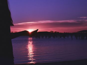 Silhouette hand by sea against sky during sunset