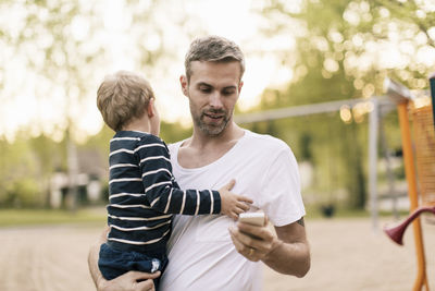 Father using phone while carrying son at playground