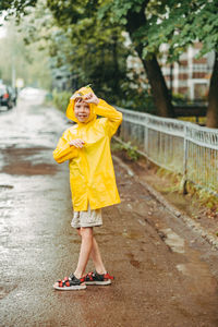 Cute boy in a yellow raincoat and sandals is having fun, running through the puddles, in the city