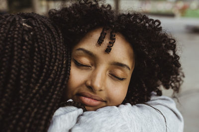 African teenage girl embracing female friend outdoors