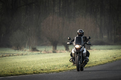 Man riding motorcycle on road against bare trees