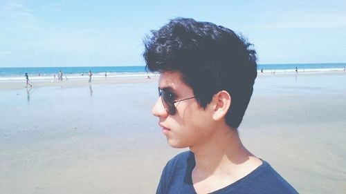 Profile view of young man standing at beach against sky