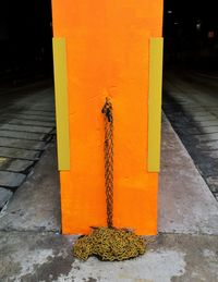 Close-up of yellow metal on footpath against orange wall