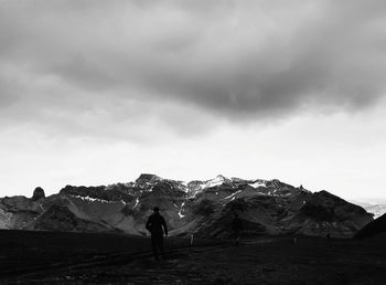 Rear view of person standing on snowcapped mountain against sky