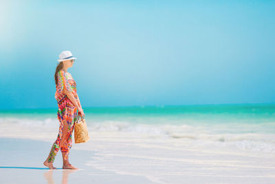 Side view of woman wearing hat standing on beach