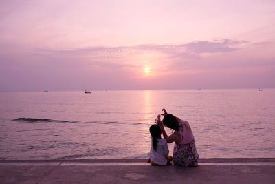 Woman sitting on sea against sky during sunset