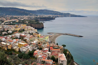 High angle view of residential district by sea against cloudy sky