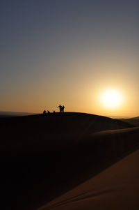 Silhouette people at desert against clear sky during sunset